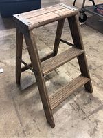 Two-step wooden step ladder positioned at an angle on concrete floor, showing side and step surfaces