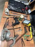 Wide shot of assorted tools on wooden surface including socket set, drill, lights, pulleys and various hand tools.