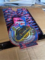 Box containing multiple Pepsi branded micro skateboard key chain packages, showing numerous units tightly packed.