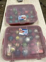 Two pink translucent plastic storage boxes stacked on top of each other, containing Christmas ornaments inside.