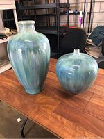 Photo showing two coastal style vases on wooden table, one tall and one round, both with blue aqua glaze.
