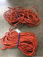 Two long orange extension cords coiled and tied with blue ties, laid on a gray floor.