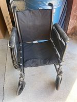 Front view of wheelchair showing black fabric seat and backrest, armrests, and front caster wheels