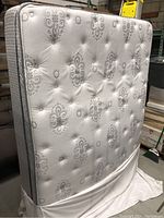 Queen size pillow top mattress standing upright showing the white and gray patterned floral design with tufting on the surface.