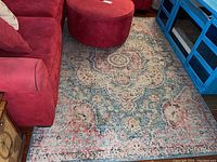 Area rug on hardwood floor between red upholstered furniture and blue shelving unit, showing full pattern and color tones.