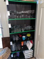 Full view of the black five-shelf unit filled with various types of glassware and kitchen items. Shelf edges have green trim.