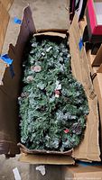 7.5 ft artificial Christmas tree disassembled in original cardboard box, showing green branches and pinecones with frosted tips.