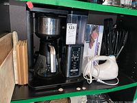 Photo showing Ninja coffee maker with glass carafe, clear water reservoir, white hand mixer, and three wooden cutting boards beside them.