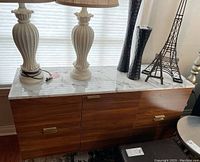 Front view of wooden storage chest with marble look top and decor items on top including two table lamps, Eiffel Tower decor, and black vases.