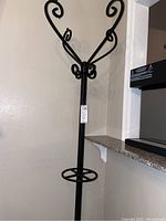 Black metal hat/coat stand showing upper decorative hooks and circular ring feature on the pole