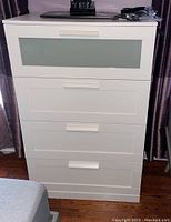 Front view of white four drawer chest showing frosted glass panel on top drawer and white handles.