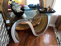 Front angle view of glass top sofa table showing wave patterned base and glass top with objects on surface.