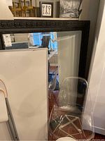 Full view of the large decorative mirror displaying the intricate black frame and sizable mirror glass in a room setting with some furniture around.