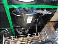 Photo showing two shelves with assorted metal pots and pans, some with lids and a metal strainer basket on top shelf.