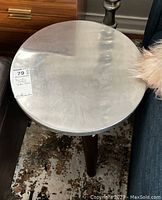 Full view of the round metal top side table showing the metal surface and wooden legs in a living room setting.