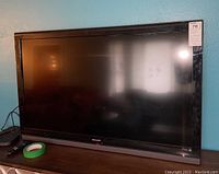 Front view of Sharp 42 inch television on the stand with remote visible next to it.