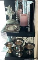 Lower shelf view showing three silverplate candle holders or small bowls with patina and frosted glass figurine.