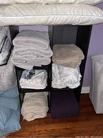 Front view of the six compartment storage shelf filled with household textiles not included in lot.