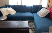 Blue upholstered sectional sofa and lounger with silver-toned legs and white fluffy and blue accent pillows in bright room