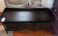 Front view of the storage bench showing the top surface, metal scroll legs, and three wicker basket drawers.