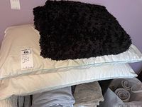 Two white pillows with light blue piping and black fuzzy decorative pillow on top