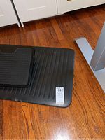 Photo of large black under desk mat with ribbed surface corner shown on wood floor.