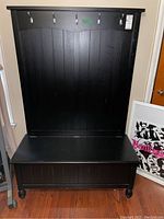 Front view of black storage bench showing vertical panel design and five hooks on back panel.