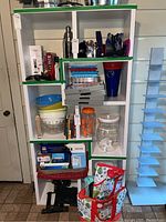 Full front view of white shelving unit holding various household items to show structure and dimensions, with green edge trim on some shelves.