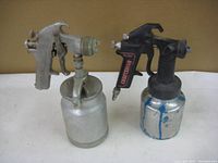 Front view of the two air paint spray tools side by side against a plain background. One silver Craftsman gun and one black DeVilbiss gun with paint containers attached.