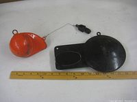 Top-down view of two downrigger weights: a black pancake style and an orange cannonball style with a ruler for scale.