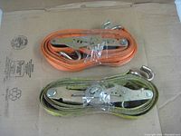 Two coiled heavy duty tie down straps, one orange Liftall Load Hugger 12' x 2", other yellow/black Loadlok 18' x 1.25"