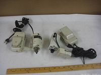 Two sewing machine motors and two foot pedal controls placed side by side with ruler for size reference