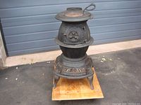 Overall front left angle view of black cast iron pot belly stove with round lid and vent doors, showing its stature and ornate legs.
