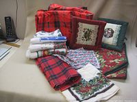 Set of Christmas linens including three red plaid placemats, quilted pot holders with holiday designs, and towels and napkins showing Christmas motifs.