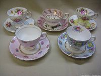 Photo of five different fine china tea cups with matching saucers featuring floral patterns and gold trim seen from above on table