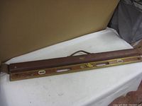Full length view of the wooden level with brass edges and carrying strap, showing used condition and brand markings.