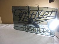 Front view of Miller High Life neon sign on glass panel. Shows neon tubing with 'Miller' in cursive and 'High Life' below in block letters.