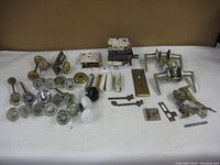 Overview photo of the entire lot showing various door knobs, glass knobs, metal knobs, locks, latch plates and strikes laid out on a table.