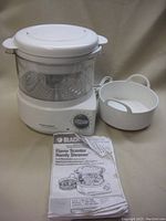 Full view of the Black & Decker Flavor Scenter Handy Steamer with heating base, clear steaming basket and white lid, along with the instruction manual and white tray.