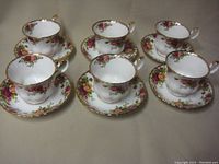 Top-down view of 6 teacups with matching saucers arranged in two rows, showing floral rose pattern and gold trim on each piece.
