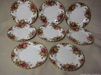Overhead view of 8 Royal Albert dessert plates arranged on a flat surface showing floral pattern and gold rim.