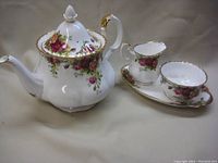 Group photo of teapot, creamer, sugar bowl, and dish in Old Country Rose pattern with gold trim.