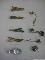 Overview image showing five tie clips and one pair of cufflinks with attached lapel pins on a plain background