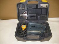 Electric hand planer in hard plastic carrying case with accessories inside the lid compartments. The planer has a cord wrapped in the main case cavity.