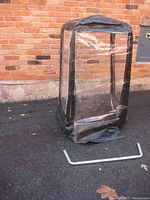 Universal snowblower cab upright against a brick wall with a separate metal frame piece on the ground