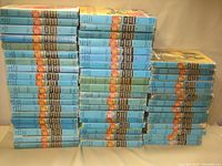 Stacked vintage Hardy Boys books with blue dust jackets viewed from front and slightly side angle, showing many volumes in the set.