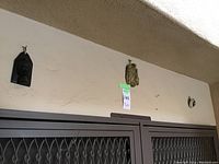 Two African mask wall decorations hung on a beige wall above a vent area, item tag showing quantity as 3 pcs.