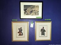 View of the three Asian art pieces hung on a blue wall. Two artworks are vertically framed with gold-tone frames depicting colorful Asian statues on cream mats. Above them is one horizontal art print framed in black showing an Asian traditional scene with people and a structure.