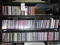 Front view of black wooden CD rack fully loaded with assorted jewel case CDs on several shelves.