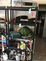 Shelving unit displaying various items including black Spalding croquet bag, camping equipment, paint cans, spray paint bottles, and other small items.
